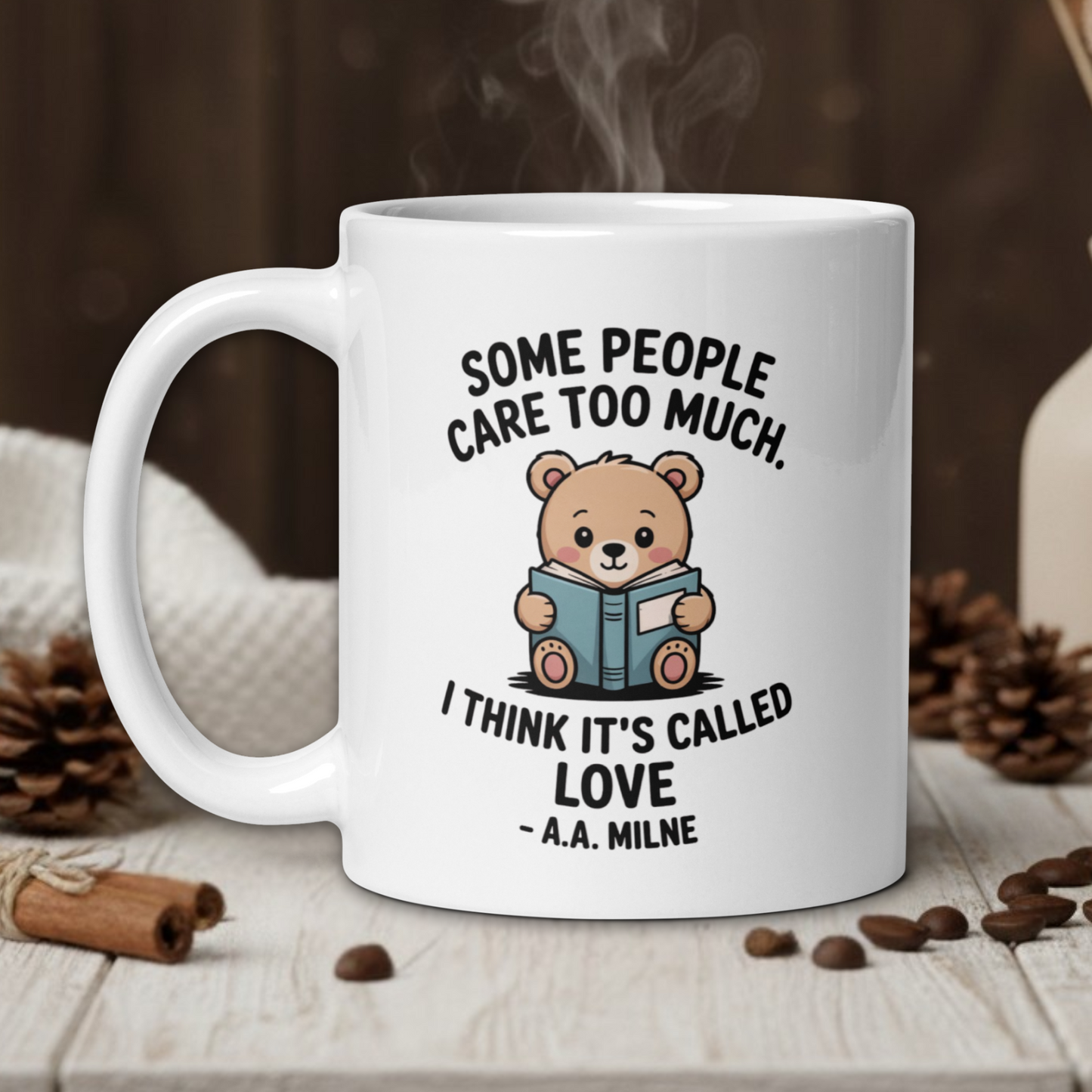 White mug with teddy bear graphic and text on a wooden table with coffee beans and a vase in the background.