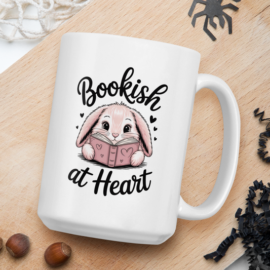 White mug with a bunny reading a book design and 'Bookish at Heart' text on a wooden board.