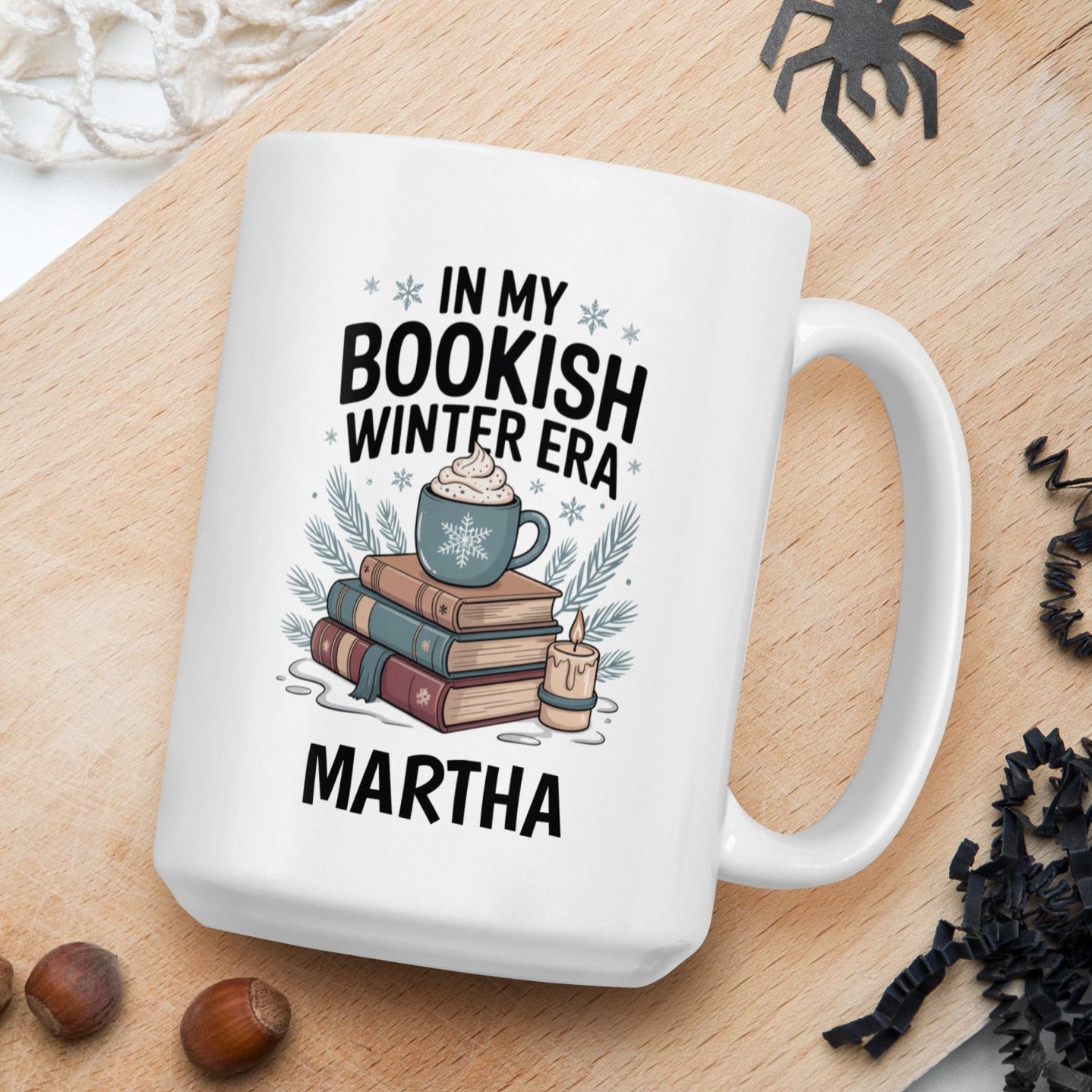 White mug with 'In my bookish winter era' design on a wooden board with nuts and spider decorations.