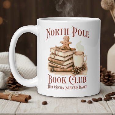 White mug with 'North Pole Book Club' design featuring books, a cup, and gingerbread man on a wooden table with coffee beans and cinnamon sticks.