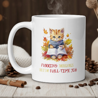 White mug with a cat illustration and text on a wooden table with coffee beans and a vase.