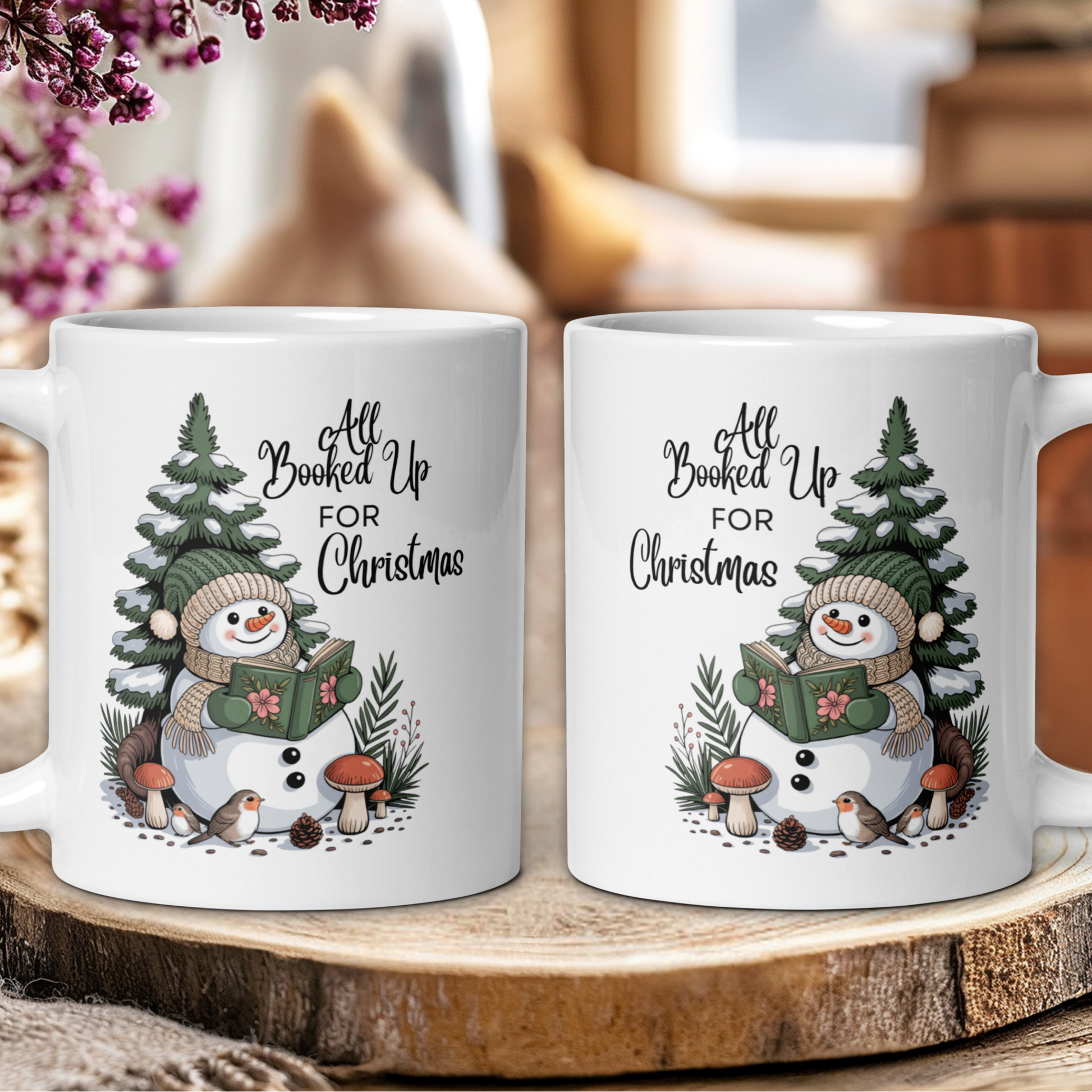 Two white mugs with a snowman design and text 'All Booked Up For Christmas' on a wooden surface.