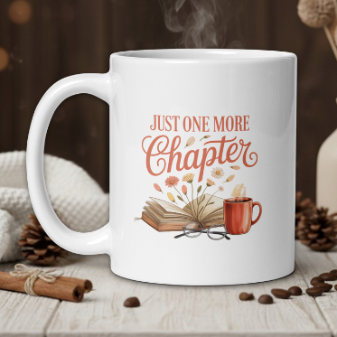 White mug with 'Just One More Chapter' design on a wooden table with coffee beans and a vase in the background.