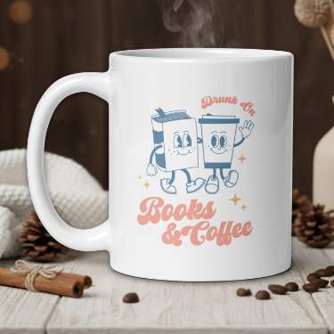 White mug with cartoon design and text 'Drunk On Books & Coffee' on a wooden table with coffee beans and a vase.