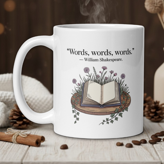White mug with Shakespeare quote and book design on a wooden table with coffee beans and a vase in the background.