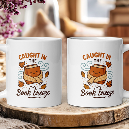 Two white mugs with a cartoon book character and text 'Caught in the Book Breeze' on a wooden surface.