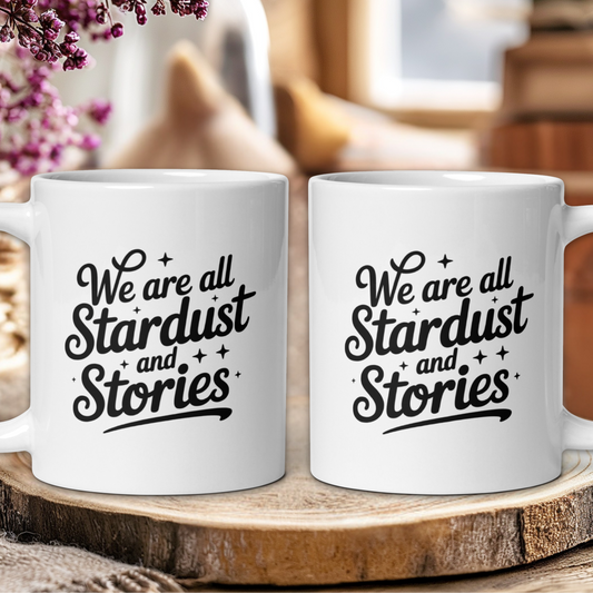 Two white mugs with 'We are all Stardust and Stories' text on a wooden surface.