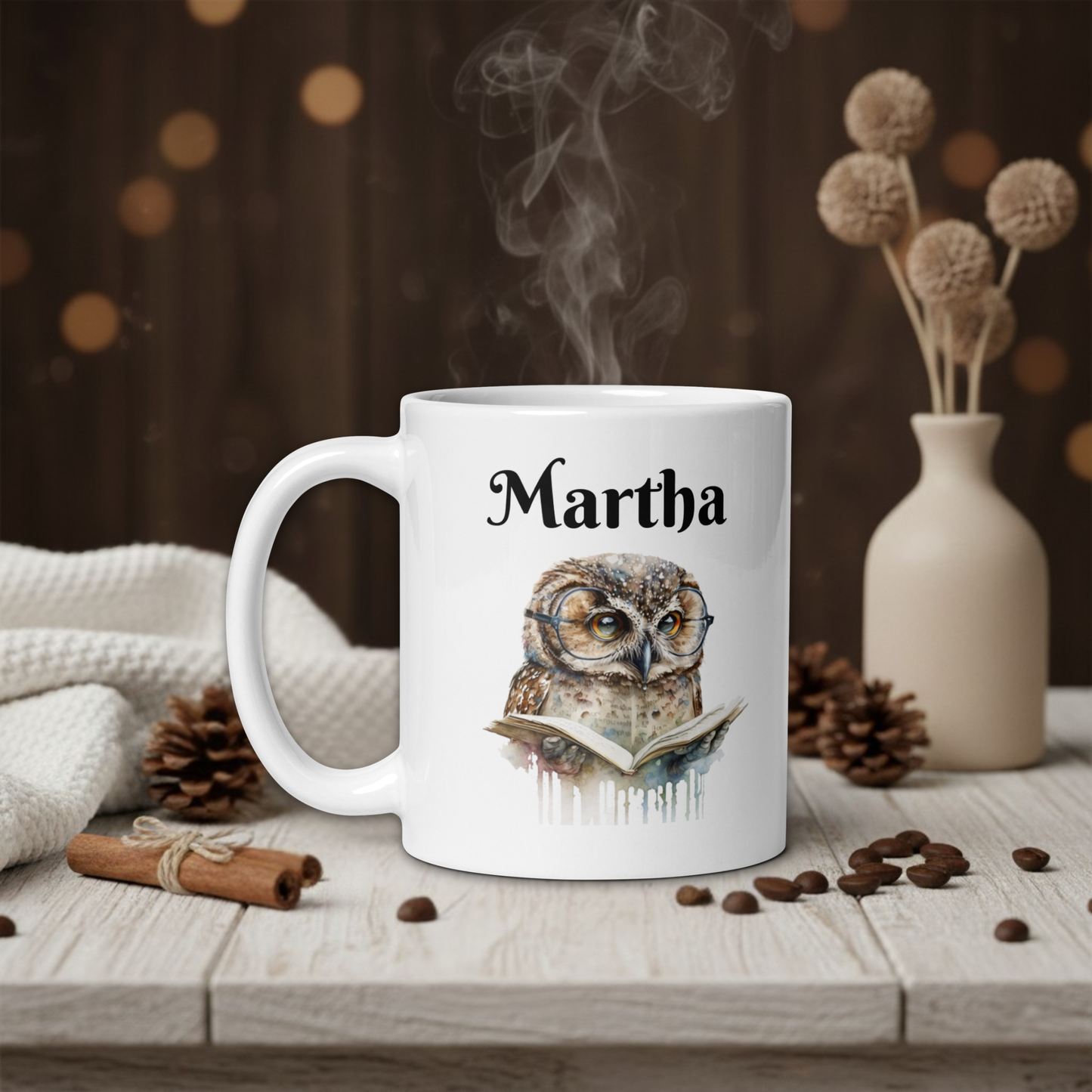 White mug with owl design and 'Martha' text on a wooden table with coffee beans and a vase in the background.