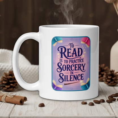 White mug with 'To Read is to Practice Sorcery in Silence' design on a wooden table with coffee beans and a vase in the background.