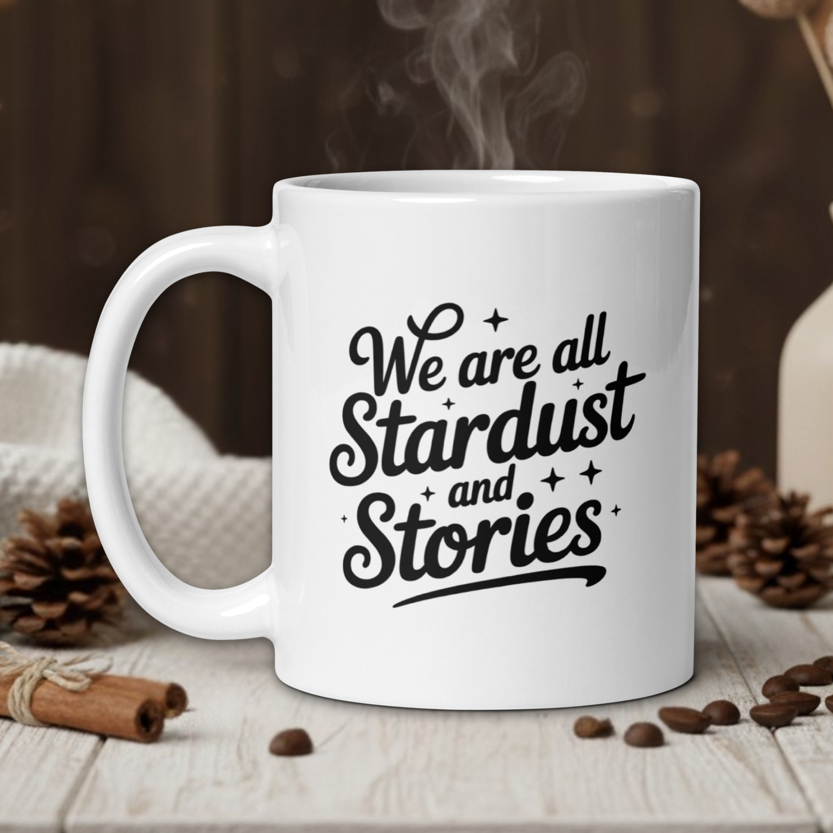 White mug with 'We are all Stardust and Stories' text on a wooden table with coffee beans and a vase in the background.