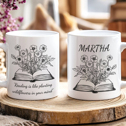 Two white mugs with floral and book designs on a wooden surface.