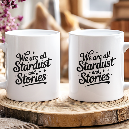 Two white mugs with 'We are all Stardust and Stories' text on a wooden surface.