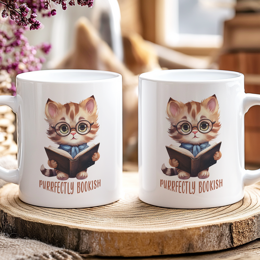 Two mugs with a cat illustration and 'Purrfectly Bookish' text on a wooden coaster.