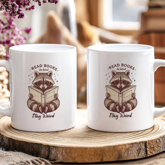 Two white mugs with raccoon illustrations and text on a wooden coaster.