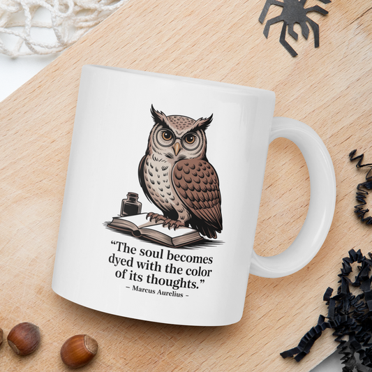 White mug with owl design and quote on a wooden board with nuts and spider decorations.