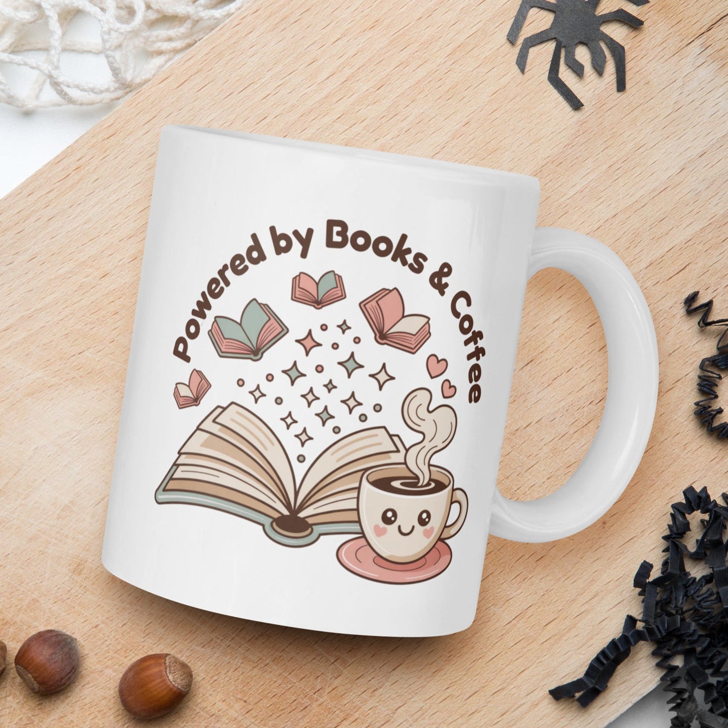 White mug with 'Powered by Books & Coffee' design on a wooden board with nuts and spider decorations.