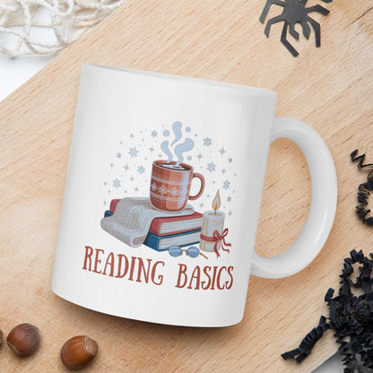 White mug with 'Reading Basics' design on a wooden board with nuts and spider decorations.