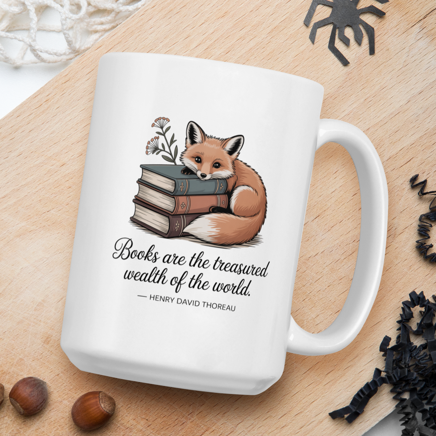 White mug with fox and books design on a wooden board with nuts and spider decorations.
